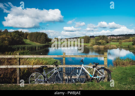 Due biciclette parcheggio vicino al recinto di fronte al pittoresco lago. Autunno a Bathgate, West Lothian, Scozia Foto Stock