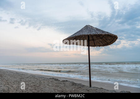 Tramonto sul mare solitario con sabbia, onde e ombrellone Foto Stock