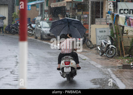 Due persone in sella a una motocicletta con un ombrello durante una pioggia monsonica, Hoi An, Vietnam Foto Stock