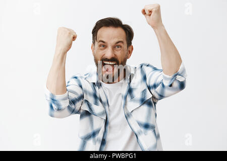 Yeah accendono vinceremo. Ritratto di felice e gioiosa emotiva europei maturi ragazzo con la barba e capelli scuri, alzando i pugni alta e urla, trionfante o il tifo mentre si guarda la partita di calcio in pub Foto Stock