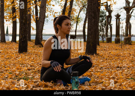 Una donna attraente in abbigliamento sportivo facendo esercizi sportivi in natura contro il tramonto e il fiume di Amur, ama la ginnastica, massaggia le gambe. Attivo giovane ragazza impegnate nello sport, conduce uno stile di vita sano. Foto Stock