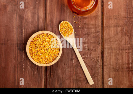 Un sano cibo biologico. Polline di api, un vasetto di miele e un cucchiaio di legno, girato da sopra al buio su un sfondo di legno con un posto per il testo Foto Stock