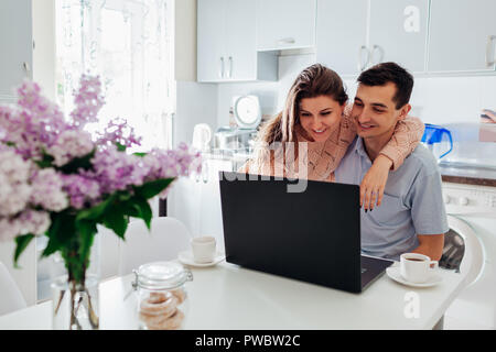 La famiglia felice coppia utilizzando laptop mentre si consuma la colazione nella cucina moderna. Giovane uomo e donna controllare social network news Foto Stock