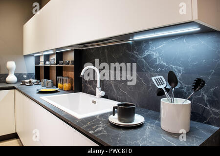 Effetto Marmo bancone cucina con utensili e di un bianco lavabo rettangolare sotto la parete montati armadi e splash back Foto Stock