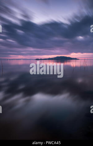 Tramonto sul lago Trasimeno, giorno nuvoloso. Come specchio di riflessione. Paesaggio italiano. Foto Stock
