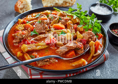 Deliziosa carne di manzo e Okra stufata o Zuppa servita in una ciotola con cucchiaio, su un calcestruzzo di colore grigio nella tabella con la ciabatta pane, vista da sopra, close-up Foto Stock