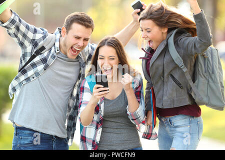 Tre studenti entusiasti di controllo qualità degli esami online in uno smart phone Foto Stock