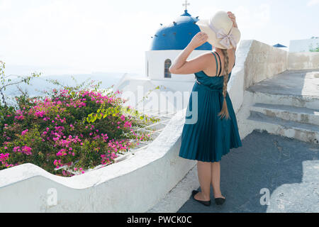 Donna felice in abito verde e cappello per il sole godendo le vacanze sull'isola di Santorini, Grecia. Vista sulla Caldera e sul Mar Egeo da Imerovigli. Foto Stock