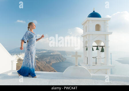 Donna felice in bianco e azzurro vestito godendo le vacanze sull'isola di Santorini, Grecia. Vista sulla Caldera e sul Mar Egeo da Imerovigli. Foto Stock