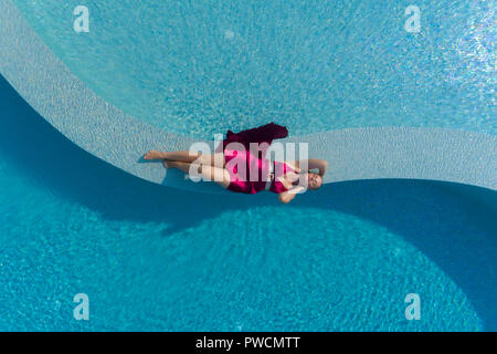 Giovane donna bionda in abito rosso giacente in piscina Foto Stock