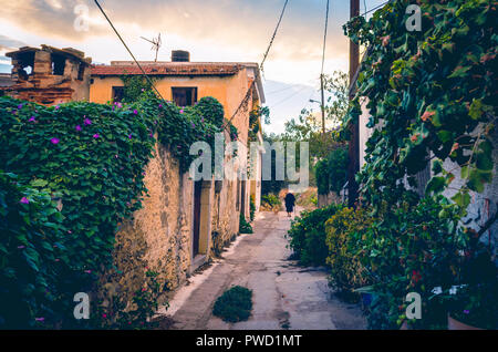 Bella vista in stile vintage di vicolo stretto con la vecchia casa, fiori colorati e un tradizionale anziani donna vestita di nero in un villaggio in cr Foto Stock