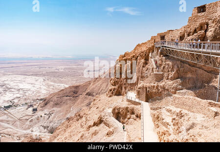 I turisti all'entrata principale dell' antica fortezza di Masada che mostra la parte superiore del percorso di serpente e la funivia che si affaccia sul Mar Morto Foto Stock