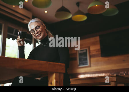 Bassa angolazione del senior donna libro di lettura e un caffè presso la caffetteria. Femmina in causals rilassante presso il cafe. Foto Stock