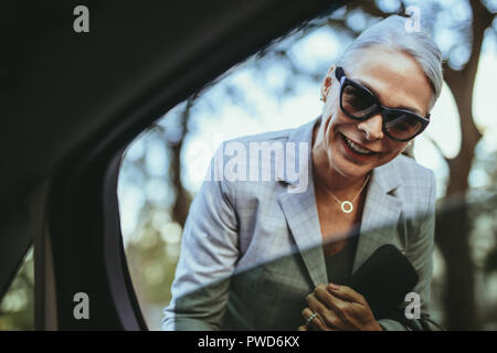 Felice senior donna che guarda all'interno dell'auto e a parlare con il conducente. Femmina nel business suit parlando con cabina conducente. Foto Stock