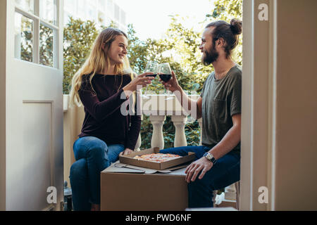 Giovane seduto nella loro nuova casa di mangiare pizza e bere vino. Matura per celebrare il loro spostamento in una nuova casa con vino e pizza. Foto Stock