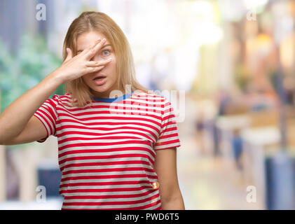 Giovane donna caucasica su sfondo isolato peeking in stato di shock che copre il viso e gli occhi con la mano, guardando attraverso le dita con imbarazzo espressione. Foto Stock