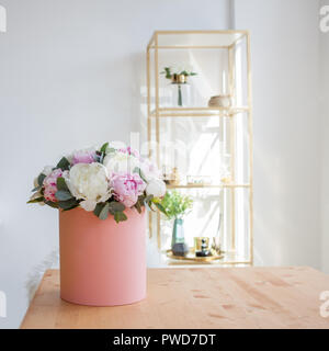 Consegna fiori per l'ufficio. Spazio di lavoro, tavolo con notebook e riviste. Un lussuoso bouquet di peonie in un cappello rosa box. Foto Stock