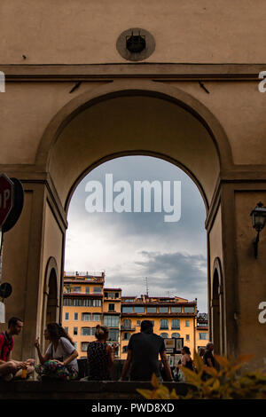 Turisti che si godono una calda serata estiva guardando l'Arno attraverso un arco impostato sotto il Corridoio Vasariano a Firenze, Italia. Foto Stock