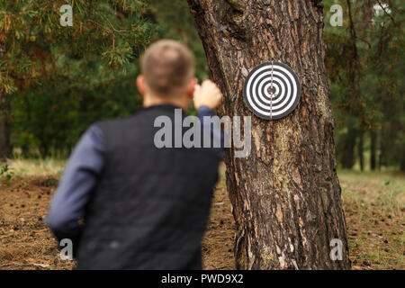 L'uomo getta freccette. Il bersaglio è appeso a un albero in aria aperta Foto Stock