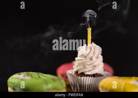 Iced tortina con il fumo di candela circondato da vetrate colorate le ciambelle in un basso angolo di visione Foto Stock