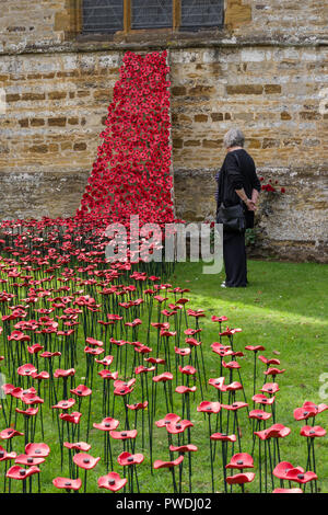 Senior donna guardando un display artigianale di papaveri in ceramica per il centenario di WW1, la chiesa di San Pietro e San Paolo, Northampton, Regno Unito Foto Stock