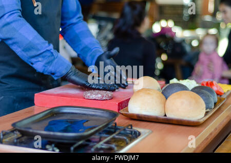 Lo chef prepara un burger sul tavolo nel ristorante.Ha le mani in guanti neri. Foto Stock