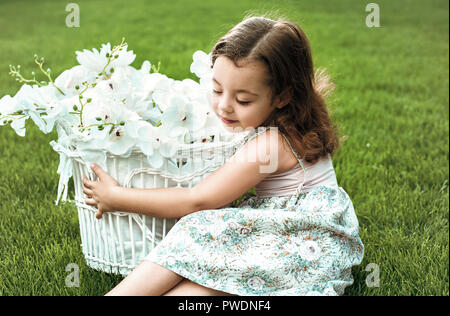 Sweet little girl tenendo un cesto pieno di fiori Foto Stock