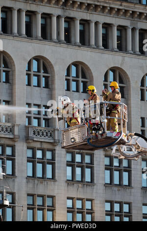 I vigili del fuoco del Regno Unito utilizzando i loro il tubo flessibile su un alta la scaletta della piattaforma girevole. Foto Stock