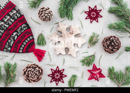 Stile nordico decorazioni di Natale. Maglia rossa inverno hat, verde rami di pino, coni e stelle, su sfondo di calcestruzzo. Foto Stock