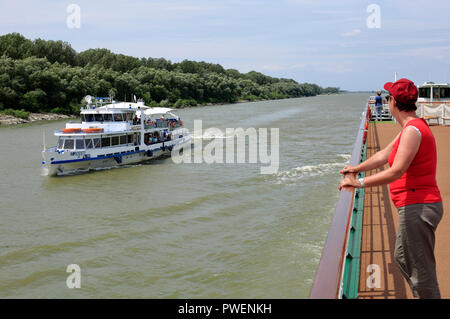 La Romania, Tulcea contea, Dobrudja, Dobruja, il Delta del Danubio, Riserva della Biosfera del Delta del Danubio, sul delta del fiume, estuario del fiume Danubio in bocca al Mar Nero, Danubio crociera, navigazione sul Danubio, aROSA cruiser Mia sul ramo di Sulina del Danubio tra Sulina e Maliuc, giovane donna si erge sulla ringhiera upperdecks avendo cura di una piccola nave di escursione, turistico, turistico, Danubio paesaggio, paesaggio fluviale, dalle rive del Danubio, bosco, Sito Patrimonio Mondiale dell'UNESCO, monumento naturale Foto Stock