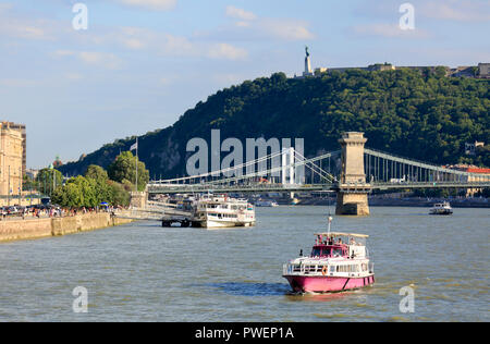 Ungheria Ungheria centrale, Budapest, Danubio, Città Capitale, Danubio paesaggio con motoscafo e cruiser, dietro la Istvan Ponte delle catene di Szechenyi e il Ponte Elisabeth tra Pest e Buda, sullo sfondo la collina Gellert con il monumento della libertà e la statua della Libertà, crociera sul Danubio, navigazione fluviale, Patrimonio Mondiale dell UNESCO Foto Stock