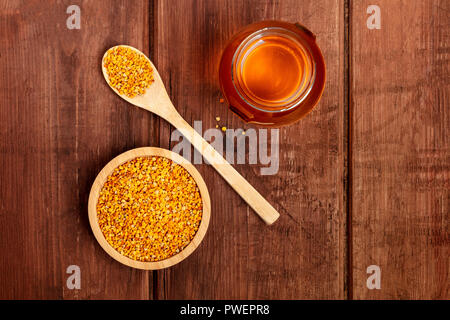 Un sano cibo biologico. Polline di api, un vasetto di miele e un cucchiaio di legno, girato dalla parte superiore su di un legno scuro dello sfondo con spazio di copia Foto Stock