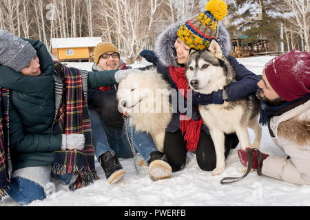 A piena lunghezza Ritratto di felice giovani giocando con due cani all'aperto nella neve mentre godendo il tempo in inverno resort Foto Stock