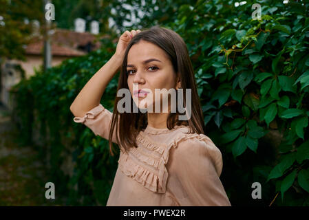 Giovane donna in posa di un beige camicetta alla recinzione di pietra coperto con foglie. Foto Stock