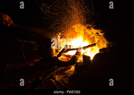 Immagine di un grande falò attorno al quale la gente crogiolarsi nelle montagne di notte Foto Stock