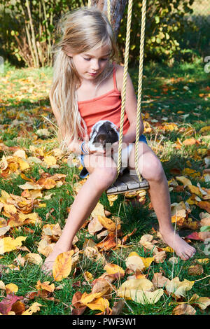 Carino bambino ragazza seduta in altalena in giardino e giocare con la cavia animale da compagnia Foto Stock