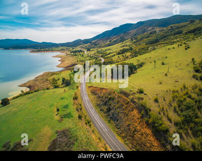 Strada rurale avvolgimento attraverso il lago e le montagne. Antenna panoramico paesaggio di Australia Foto Stock