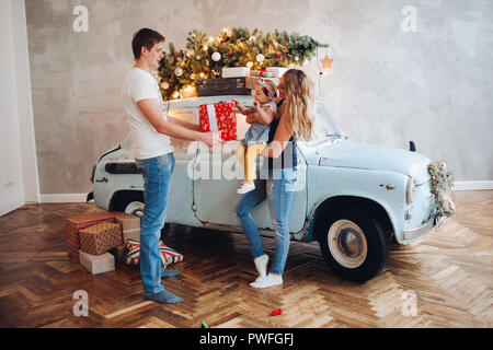 Vista del bel papà Natale dando presente, big red box, per blonde mom e poco carino figlia. Famiglia di trascorrere del tempo insieme in casa decorata f Foto Stock