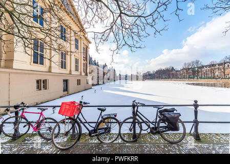 Rusty biciclette davanti alla vista panoramica del parlamento olandese edificio e la sua congelati acqua di stagno Foto Stock