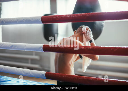 Boxer tergi sudore con asciugamano dopo dura lotta in seduta pugilato ring Foto Stock