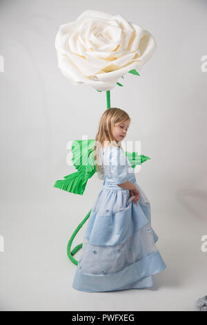 Caucasian bambina con capelli belli in un vestito blu con un simpatico sorriso che pongono la fotocamera su sfondo grigio Foto Stock