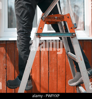 Tagliate il colpo di un uomo in equilibrio su una scala a pioli, composizione quadrata Foto Stock