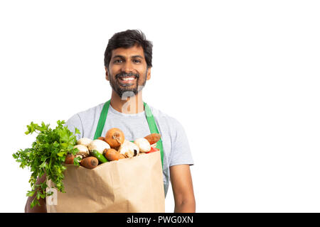 Gentile indian fruttivendolo dipendente azienda verdura fresca borsa come un sano concetto con sorriso isolato su bianco Foto Stock