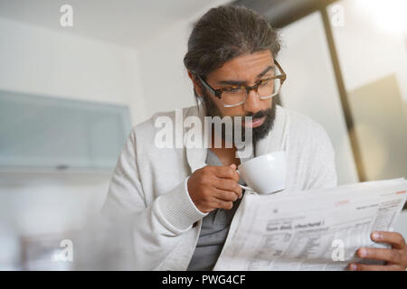 Dai capelli scuri uomo barbuto a casa leggere il giornale Foto Stock