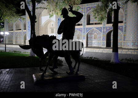 Vista di notte del profilarsi la statua di Hoja Nasruddin, un semi-mitico 'wise fool' che appare nella dottrina Sufi-racconti intorno al mondo e il XVI secolo Nadir Devanbegi Madrasah che era destinata ad essere una carovana saray, ma secondo l'ordine del righello Imam Kulimkhan, è stato ricostruito in una madrasa situato nel Labi-havz complesso considerato per essere il centro della vecchia città di Bukhara in Uzbekistan Foto Stock