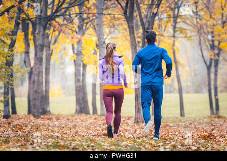 Giovane jogging in foglie colorate, visto da dietro Foto Stock