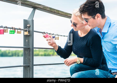 Coppia giovane guardando lucchetto appendere su parapetto Foto Stock