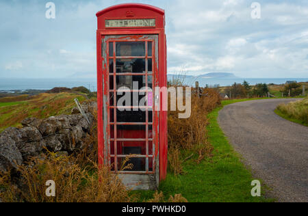 Vecchio telefono rosso scatola, abbandonati e defunta in un villaggio rurale nelle Highlands della Scozia si affaccia l'isola delle Ebridi di Eigg. Foto Stock