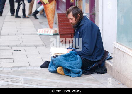 Un uomo senza tetto la lettura di un libro sulle strade di Leeds Foto Stock