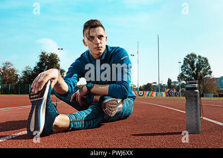 L'accoppiamento maschio runner stretching gambe la preparazione per eseguire durante la formazione a stadium tracce. L'atleta, fitness, ginnastica, sport, esercizio, formazione atletico e concetto di stile di vita Foto Stock